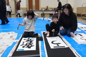 力強く筆を運んで作品を完成させる親子